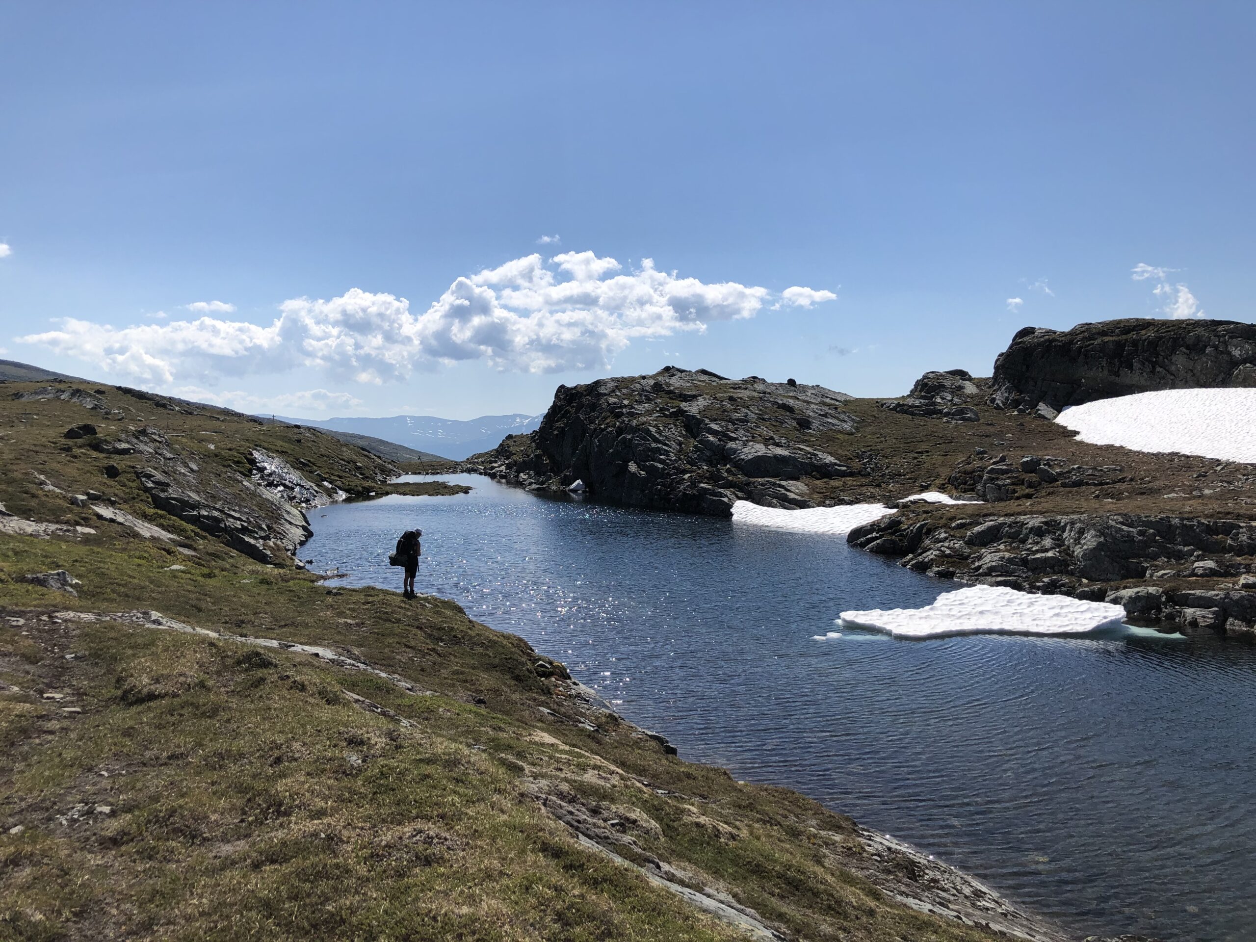 Liten människosilhuett vid tjärn uppe på kalfjället. omgiven av karga bergshällar