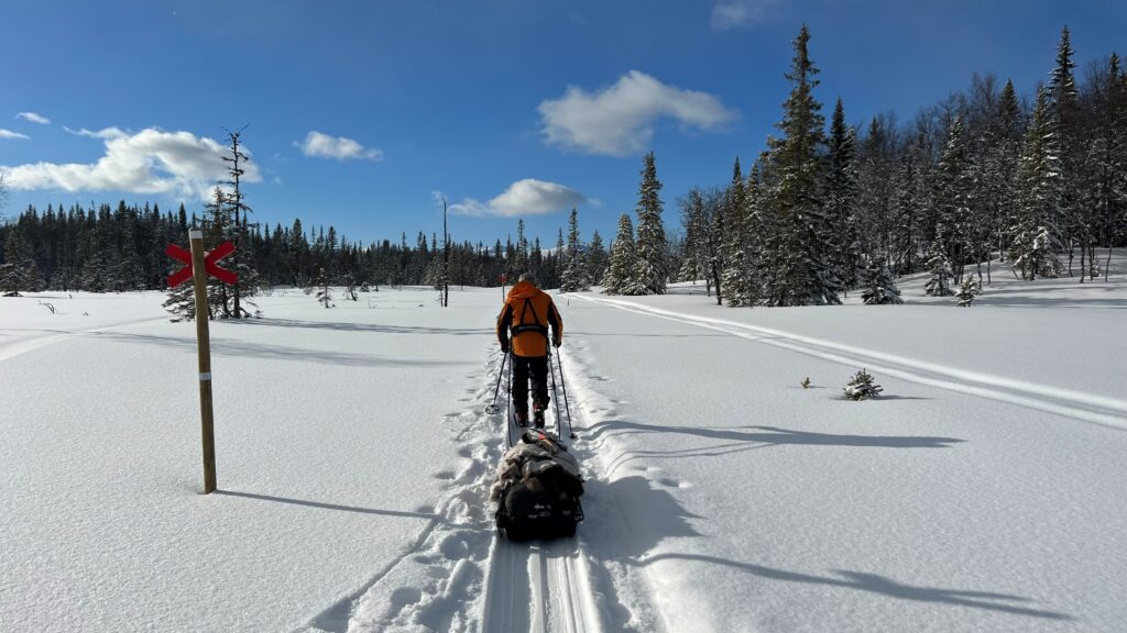 På väg längs fjälled med skidor och pulka en solig dag