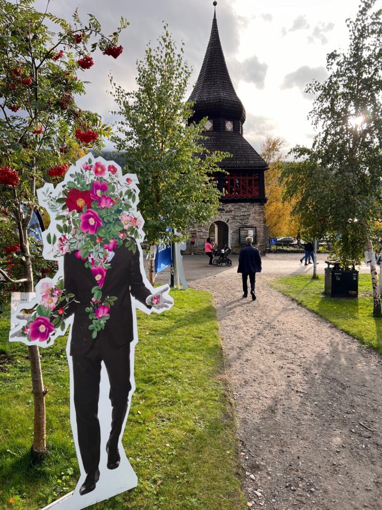 En figur som föreställer en invasiv vresros med människokropp, framför klockstapeln vid Åre gamla kyrka