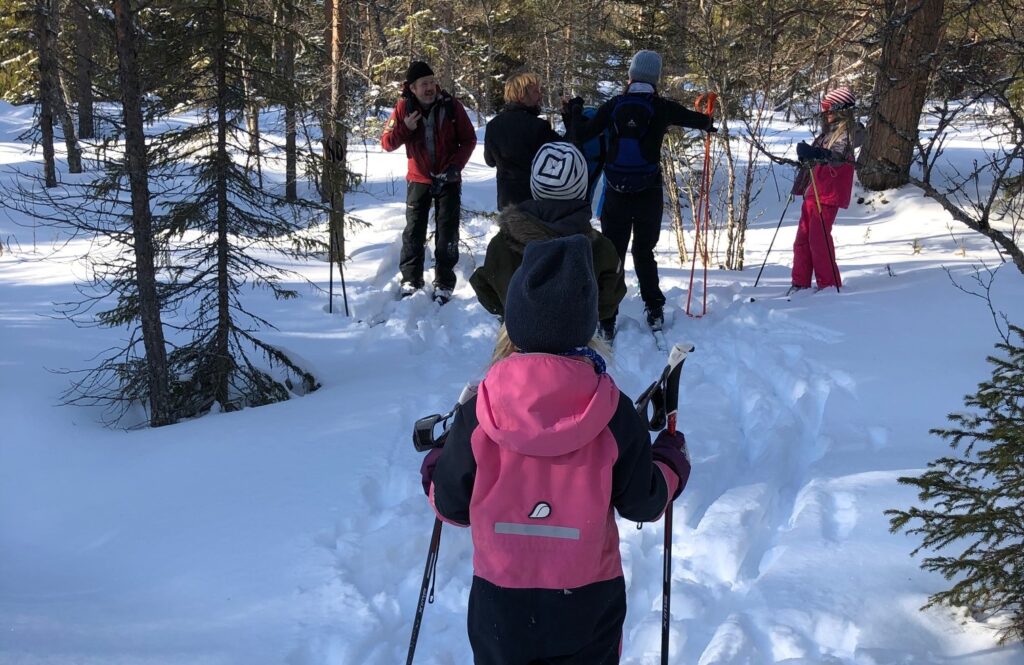 Barn i rosa skidoverall på skidtur, Tittar på en grupp människor i bakgrunden .