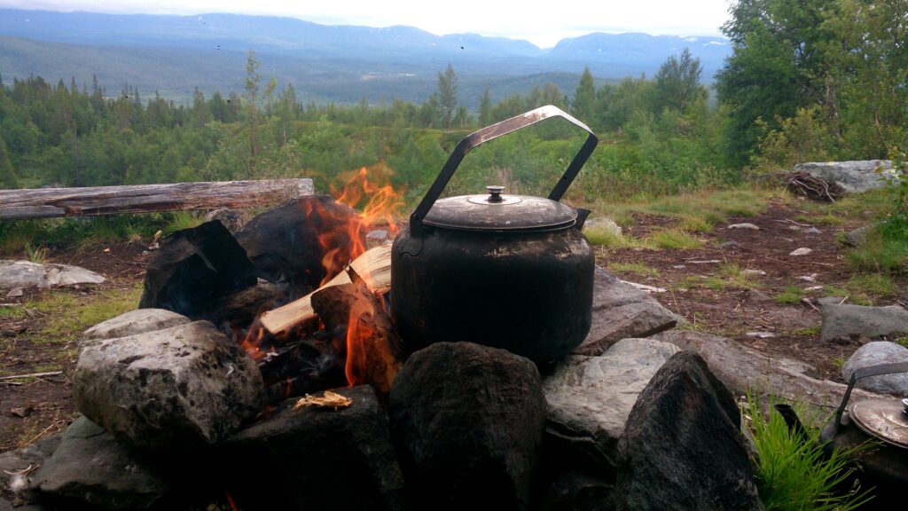 Sotig kaffepanna på eldstad av stenar med fjällkedja i bakgrunden
