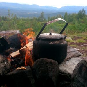 Sotig kaffepanna på eldstad av stenar med fjällkedja i bakgrunden