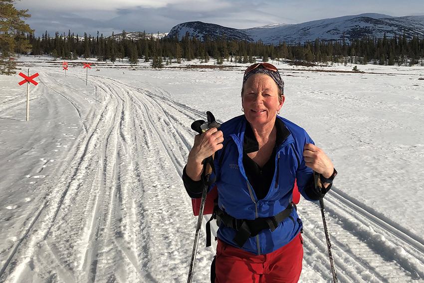 Marie ute på skidtur en solig vårvinterdag, med fjällmassiv i bakgrunden