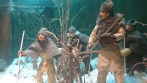 Fyra människofigurer i utställningsmonter med vintrig jaktmiljö från stenåldern
