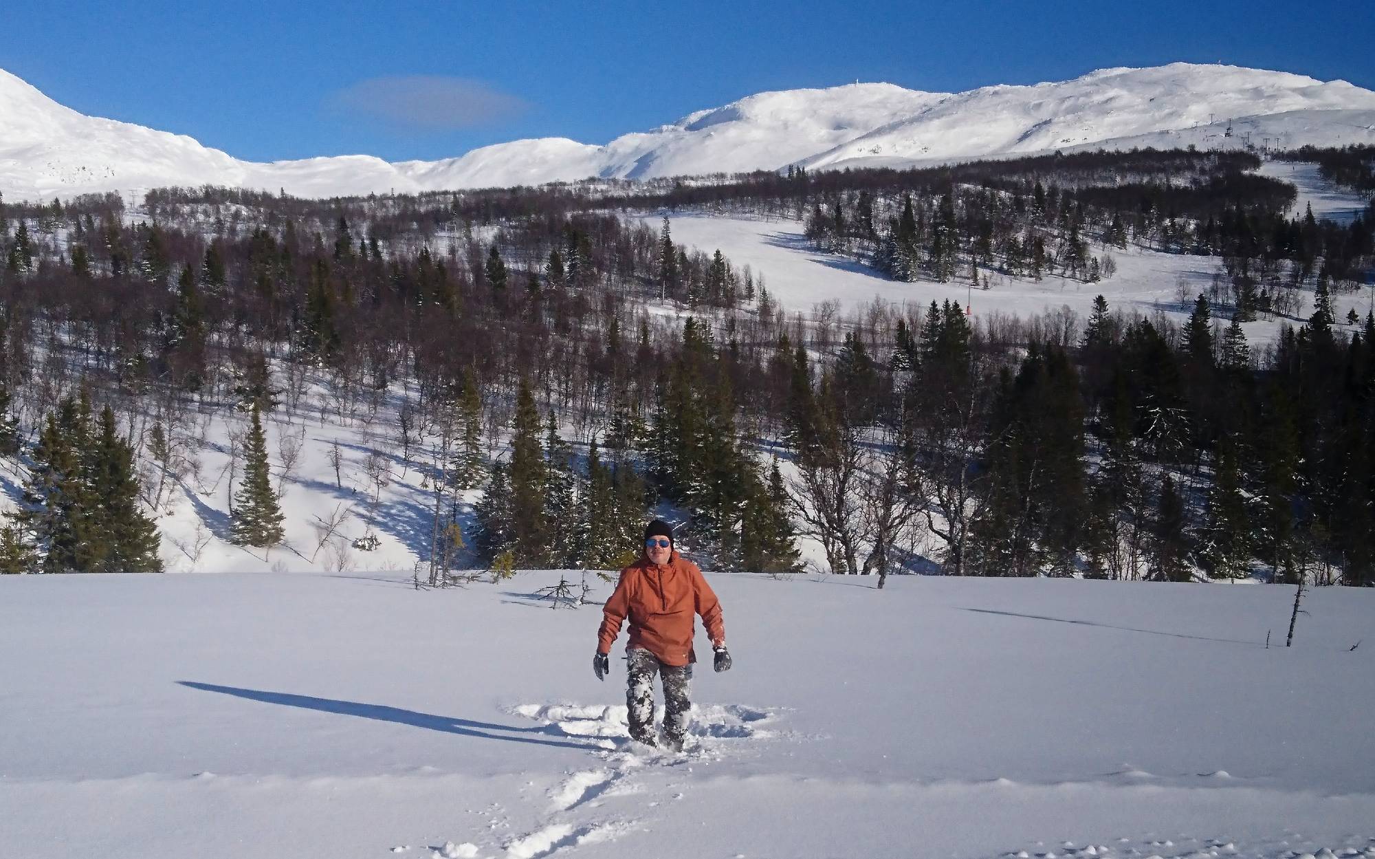 Naturums guide pulsar i djupsnö med fjäll och blå himmel i bakgrunden