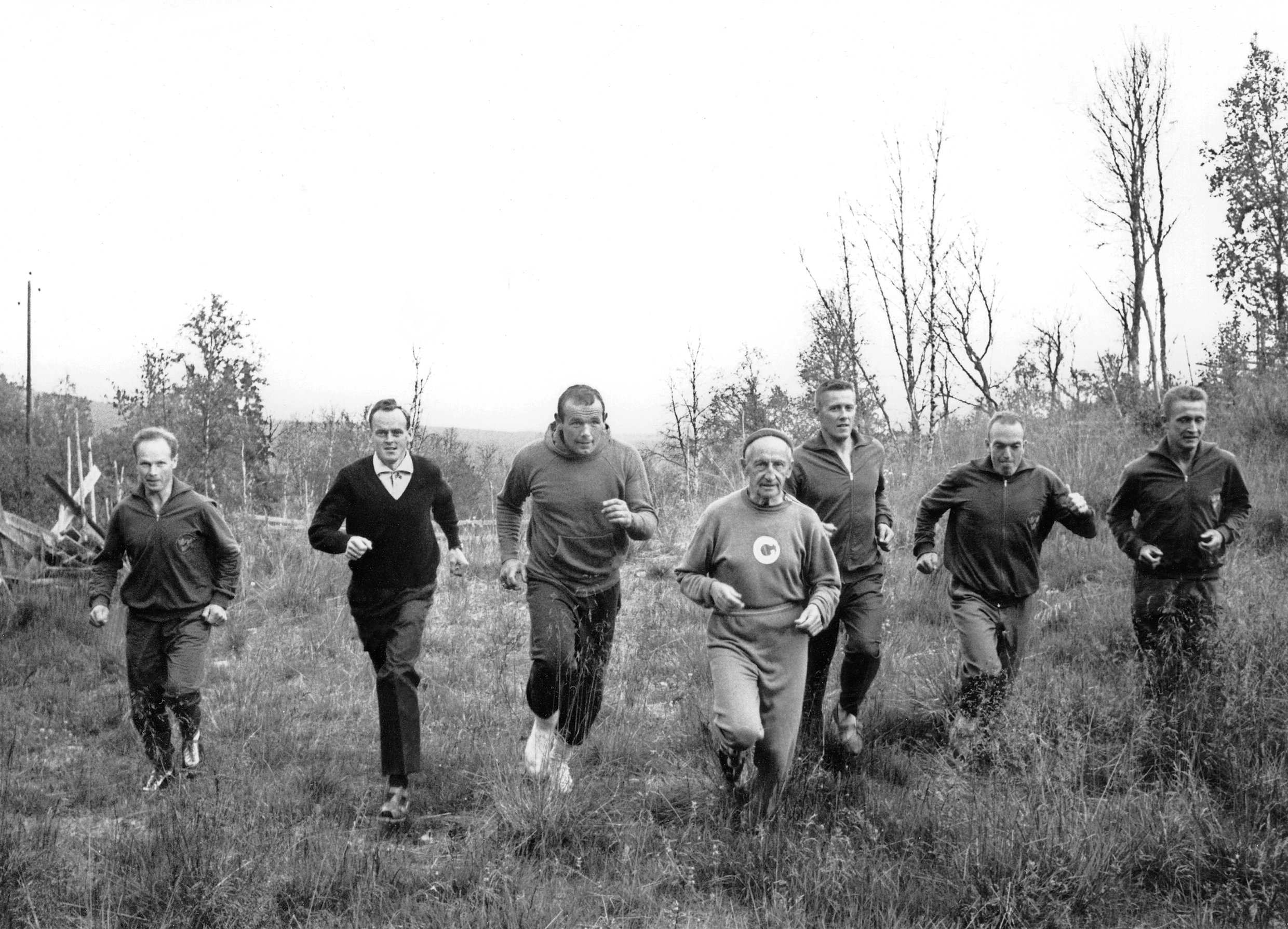 Svartvit bild av Gösta Olander och en grupp idrottsmän som joggar på en myr